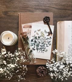 an open book sitting on top of a wooden table next to flowers and a candle