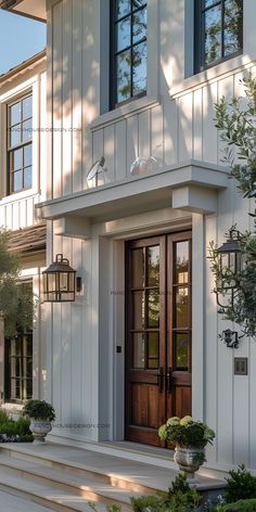 a white house with two doors and steps leading up to the front door is flanked by potted plants