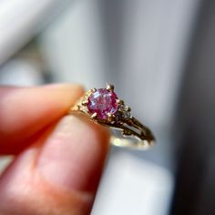 a close up of a person's hand holding a ring with a pink stone