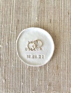 a white ceramic button with the words london and two hearts on it sitting on a piece of fabric