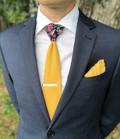 There is nothing like a versatile necktie that is solid on the front and a floral print tail to give your formal style an elegant and dapper touch. Simple and sophisticated make it the ideal neck tie to wear with most of your dress shirts and suits for any occasion.  Color:  Marigold Yellow Solid Front with Black Floral Print Tail (Back side)  Material:  100% Cotton Necktie:  approx. 2.75 inches wide and 58 inches long Pocket Square:  approx. 12 inches by 12 inches   marigold solid on one side a Yellow Suit And Tie Accessories For Black Tie Event, Dapper Gold Accessories For Black Tie Suit, Gold Suit And Tie Accessories For Wedding, Yellow Tie Outfit Men, Gold Tie For Black Tie Events, Classic Ties With Pocket Square For Groom, Classic Groom Tie With Pocket Square, Dapper Gold Tie For Business, Gold Dapper Ties For Weddings