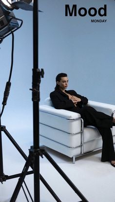 a woman sitting on a white couch in front of a camera set up for a photo shoot