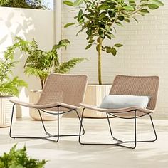 two lounge chairs sitting next to each other on a tiled floor near potted plants