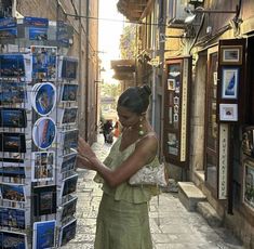 a woman is looking at pictures on display in an alleyway with people walking down the street