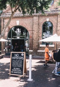 two people walking past a sign that says no hipsters on the sidewalk in front of a brick building