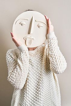 a woman covering her face with a white mask on her face and holding it up to the side