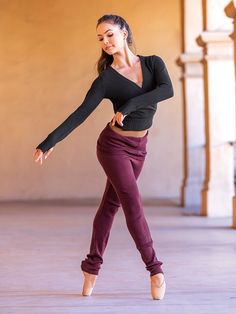 a young woman is dancing on the floor in purple pants and a black top with long sleeves