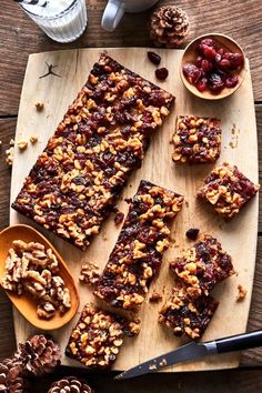 a wooden cutting board topped with granola bars next to pine cones and spoons