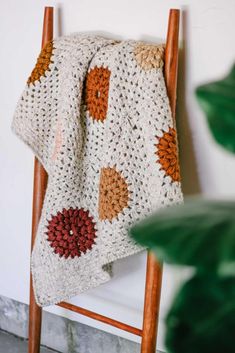 a crocheted blanket hanging on a wooden chair next to a potted plant