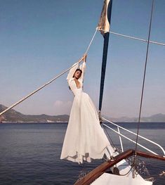 a woman in a white dress is hanging off the side of a sailboat while holding her hands up