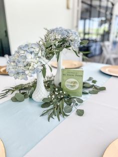 the table is set with blue and white flowers, greenery, and an open book