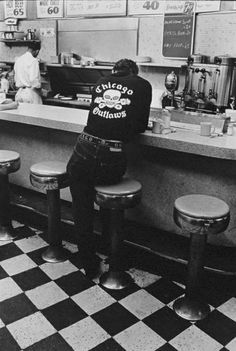 a black and white photo of a man sitting at a counter in a restaurant with stools