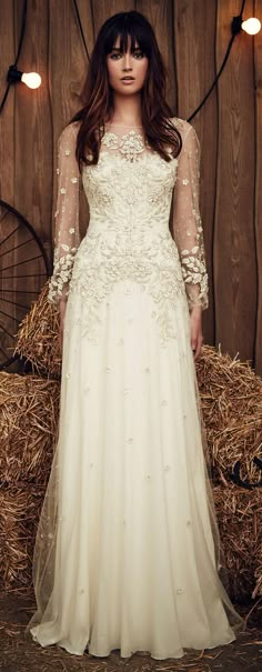 a woman standing in front of hay bales wearing a wedding dress with long sleeves