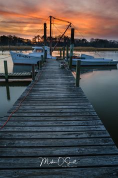 a dock with boats docked at the end and a colorful sunset in the sky behind it