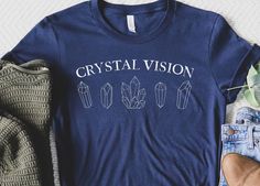 This "Crystal Vision" shirt is the perfect celestial, mystical gemstone shirt! A great good energy, moon child, witchy shirt to add to your wardrobe. If you are ordering multiple items, they may arrive separately from the printing providers. Tracking will be available to you, but please contact me if you have any questions and I will happily assist  FIT AND SIZING  ✨Bella + Canvas Unisex T-Shirt 3001 ✨Retail fit, runs true to size. Ladies should size down if you're looking for a more fitted look. ✨Shirts have a relaxed loose fit, slightly longer sleeve and body length. A size chart is available to review in the photos ✨100% Airlume combed and ringspun cotton ✨T-Shirts arrive un-rolled and un-knotted, simply folded PRINTING ✨Direct to garment printing: the ink is directly printed into the f Crystal Tshirt, Spirituality Shirts, Crystal Shirt, Witchy Cotton T-shirt For Fall, Mystical Moon Shirt, Cheap Spiritual Graphic Print T-shirt, Celestial Shirt, Witchy Shirt, Spiritual Shirts