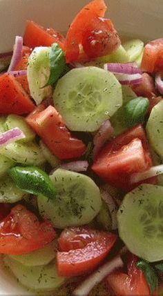 a salad with cucumbers, tomatoes and onions in a white bowl on a table