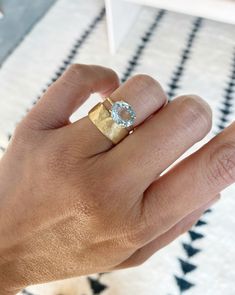 a person's hand with a gold ring on top of it and a blue stone in the middle