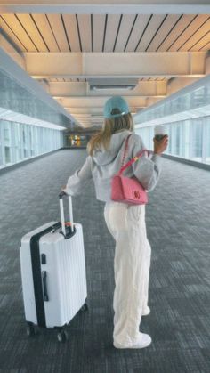 a woman is walking through an airport with her suitcase and holding a cup in one hand