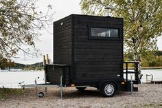 a black tiny house sitting on the side of a lake