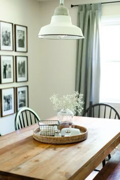 a wooden table topped with a basket filled with flowers next to a light hanging over it