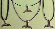 three necklaces with dolphins hanging from them on a green surface, one is purple and the other is silver