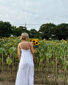 a woman in a white dress standing in front of a field of sunflowers