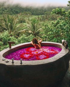 a woman is sitting in a large bath with flowers all over the tub and trees