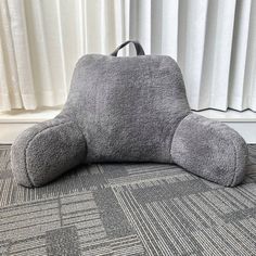 a gray teddy bear pillow sitting on top of a carpeted floor next to a window