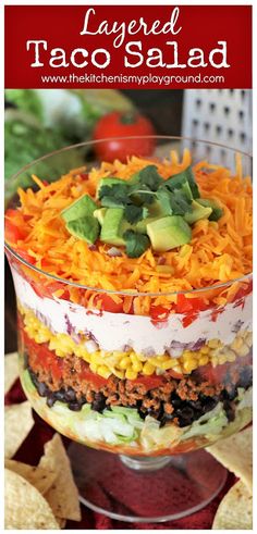 layered taco salad in a glass dish with tortilla chips on the side