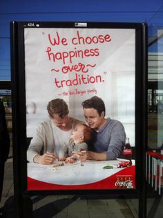 two men and a baby are sitting at a table in front of a sign that says we choose happiness over traditional