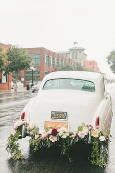 an old car is decorated with flowers and greenery in the rain on a city street