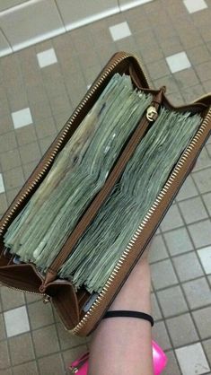 a woman's hand holding a wallet full of money in front of tiled floor