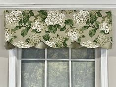 a window with a flowered valance and green leaves on the top, in front of a white wall