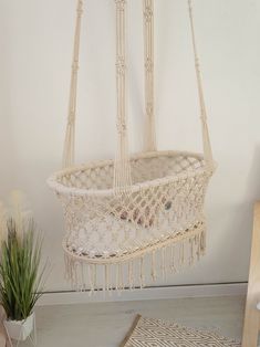 a white hammock hanging from the ceiling next to a potted plant in a room