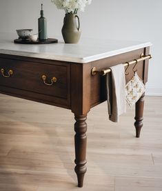 a kitchen island with marble top and brass pulls on the legs, next to a potted plant