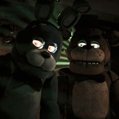 two stuffed animals with glowing eyes are standing next to each other in a dark room