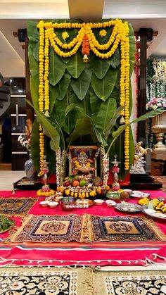 an arrangement of flowers and other decorations on a red table cloth in front of a large green plant