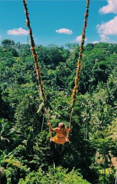 a woman is swinging on a rope in the air over some trees and greenery