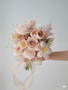 a bride's bouquet with pink flowers and white ribbons is being held by her hand