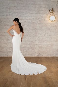 a woman in a white dress standing on a wooden floor next to a brick wall