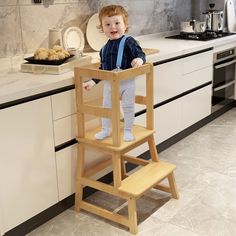 a small child standing on a wooden step stool in a kitchen next to a counter