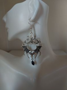 Unveil your daring side with our spellbinding Gothic Bat Earrings. Crafted in the captivating Tibetan silver style, these unique earrings feature intricately designed bats and a raised connector, all adorned with a mesmerizing black teardrop crystal. Embrace the allure of the night with our exquisitely detailed bat-shaped earrings, symbolizing mystery and transformation for those who appreciate the enigmatic. Each pair of Gothic Bat Earrings is meticulously handcrafted with skill and passion, ensuring a high level of artistry and quality. Their darkly stylish and bold design allows them to seamlessly complement various outfits, from casual wear to formal attire. For those seeking an accessory that stands out from the crowd, our Gothic Bat Earrings are the perfect choice to draw attention a Elegant Winged Metal Jewelry, Vampire Style Metal Earrings For Halloween, Halloween Vampire Metal Earrings, Vampire Style Metal Pierced Earrings, Elegant Metal Halloween Earrings, Elegant Metal Earrings For Halloween, Gothic Dangle Metal Plug Earrings, Gothic Metal Dangle Plug Earrings, Gothic Silver Metal Earrings