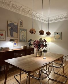 a dining room table and chairs with flowers in a vase on the end, along with art hanging from the ceiling