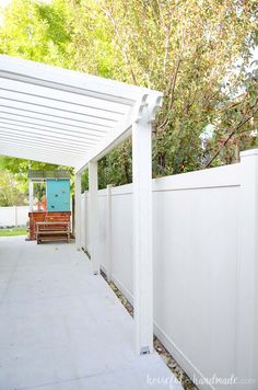 a white fence with a bench on the side and trees in the backgroud