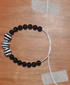 a black and white beaded bracelet sitting on top of a wooden table next to a cord