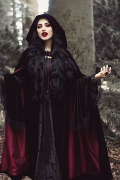 a woman dressed in black and red is standing near a tree