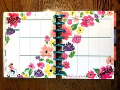 a planner with flowers on it sitting on top of a wooden table next to a pen