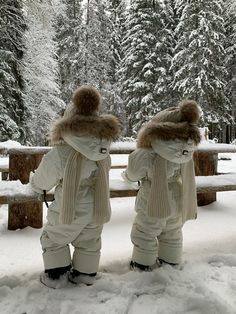 two snowboarders standing in front of a bench covered in snow and wearing winter gear