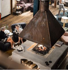 two women sitting around a fire pit in a living room next to couches and tables