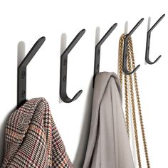 three coats hanging from hooks on a white wall next to a coat rack and scarf